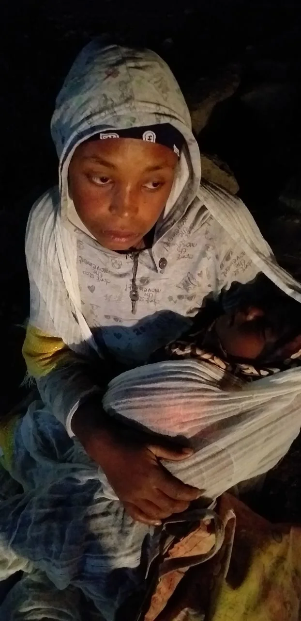 A mother and infant resting together at night under a shared wrap.