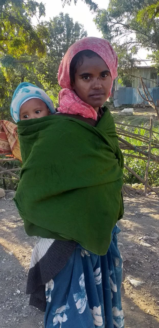 A mother carrying an infant wrapped securely against her back outdoors.